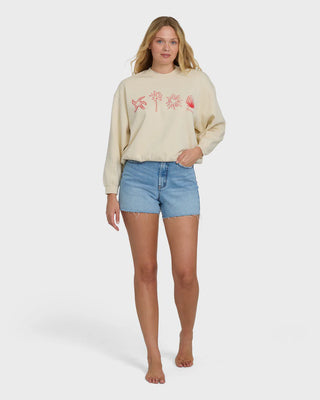 Woman wearing a beige sweater with floral designs and denim shorts on a white background