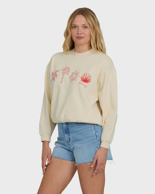 Woman wearing a beige sweatshirt with palm tree and shell designs on a white background