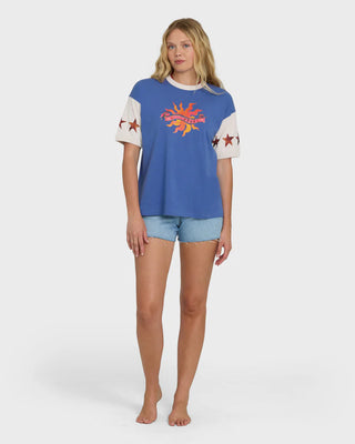 Woman wearing a blue t-shirt with a colorful graphic and denim shorts on a white background