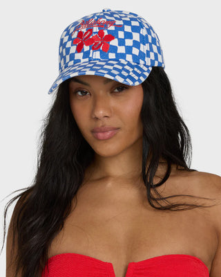 Woman wearing a blue and white checkered cap with red flowers and text, against a plain background.
