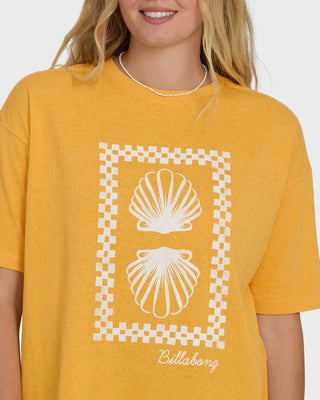 Yellow t-shirt with white shell design and 'Billabong' branding worn by a person.