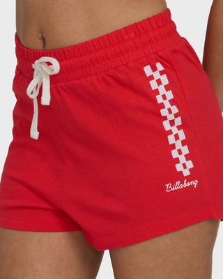 Red shorts with a white checkered pattern and brand logo on a neutral background
