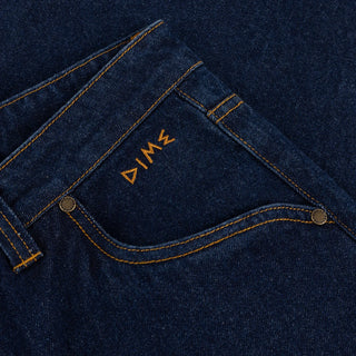 Front view of Dime Baggy Wink Denim Pants in dark Indigo with wide legs, contrast stitching, Western pockets, belt loops, and an embroidered front-pocket logo