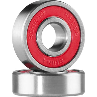 Two Bones REDS skateboard bearings displayed on a black REDS box, one showing its red rubber shield and the other its open side.