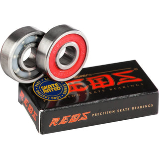 Two Bones REDS skateboard bearings displayed on a black REDS box, one showing its red rubber shield and the other its open side.