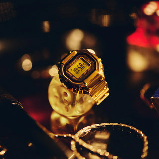 Gold Casio digital watch on a reflective surface with blurred background