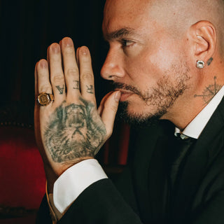 Man with tattoos on hand and face, wearing a suit and diamond earring.