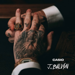 Close-up of a hand with tattoos wearing a gold Casio watch against a dark background