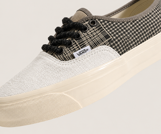 Close-up of a Vans sneaker showing the toe box, black laces, a black and beige houndstooth pattern, and a cream-colored rubber sole on a light beige background.