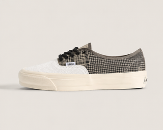 A Vans platform sneaker in a black and white patterned design, featuring a textured white toe box, black laces, and a thick cream-colored platform sole, set against a solid light gray background.