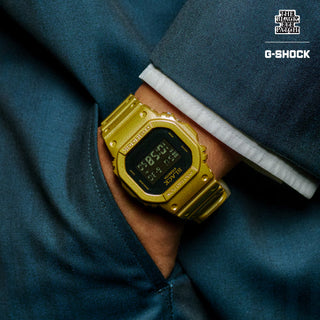 G-SHOCK DW5600BEP-9 BlackEyePatch watch with a gold-tone square case and band, black face, digital display, and BlackEyePatch branding
