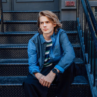 Person sitting on a set of stairs wearing a blue jacket and striped shirt.