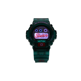 “Jae Tips G-SHOCK watch with translucent teal case and strap, lavender face, multicolor dial accents, flower graphics, and a red front button.”