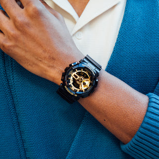 Front view of the G-SHOCK GA110GB-1A with a glossy black case and band, gold-tone layered dial, and digital displays
