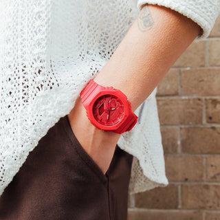 Person wearing a red watch on a blurred brick wall background