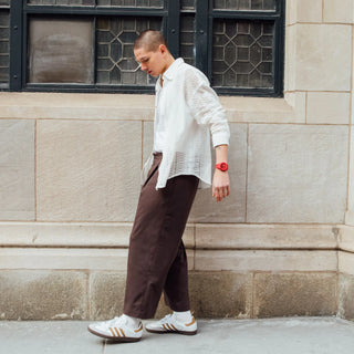 Person wearing a white shirt and brown pants standing against a stone wall.