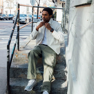 Man sitting on steps in an urban setting wearing a white jacket and green pants.