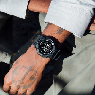 Person wearing a black digital watch on a blurred background