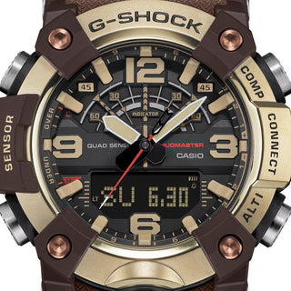 Front view of the G-SHOCK GGB100XMH-5A Mudmaster with a gold-tone bezel, dark brown case and band, black analog-digital dial, and red second hand