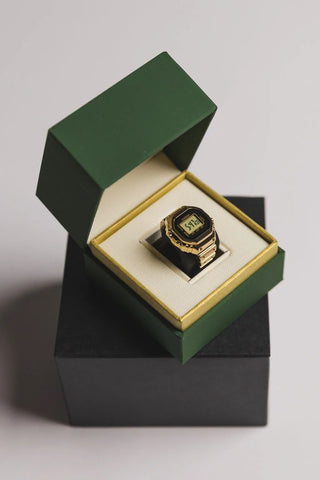 Gold ring with a digital design in an open green and black box on a light gray background