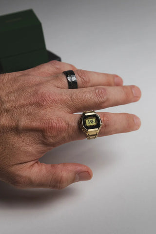Hand wearing a gold digital watch on a plain background