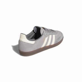A single Adidas Samba sneaker in gray suede with white three-stripes, a cream heel tab, and a brown gum sole, shown from a three-quarters angle on a white background.