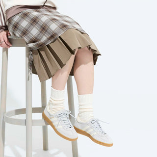 Person wearing a plaid skirt, beige pleated skirt, white sneakers, and white socks on a white background.