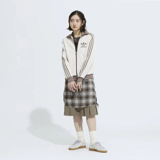 Person wearing an Adidas tracksuit with a plaid skirt on a white background