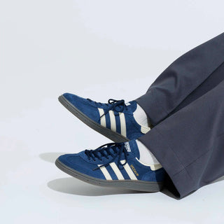 Blue Adidas sneakers with white stripes worn with a dark suit on a light gray background
