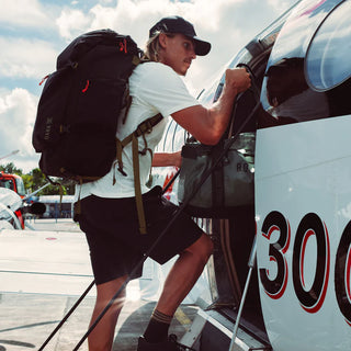 Model wearing black Roark Layover Pro Traveler Shorts with a backpack while boarding a seaplane.