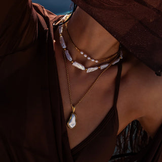 Gold necklace with glass pearl pendant and polished finish.