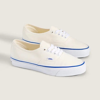 White Vans Authentic shoes with blue foxing stripe, white laces, and canvas uppers on a light neutral background.