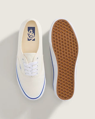 White Vans Authentic shoes with blue foxing stripe, white laces, and canvas uppers on a light neutral background.