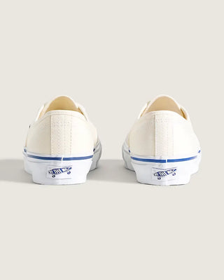 White Vans Authentic shoes with blue foxing stripe, white laces, and canvas uppers on a light neutral background.