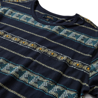 Adventurous man wearing a Roark Revival 'Sunburst Pocket Crew' knit shirt from the Mystic Motu Summer Collection, showcasing its vibrant, sunburst-inspired design and functional pocket.