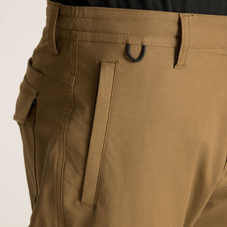 Roark Layover Pro Traveler Pants in Dark Khaki, straight-leg 4-way stretch Embarq Dura-Stretch fabric with TSA-friendly waistband, zippered travel pockets, back phone stash pocket, and laser-perforated cooling panel