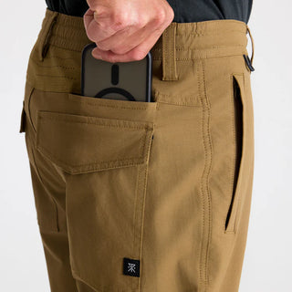 Roark Layover Pro Traveler Pants in Dark Khaki, straight-leg 4-way stretch Embarq Dura-Stretch fabric with TSA-friendly waistband, zippered travel pockets, back phone stash pocket, and laser-perforated cooling panel