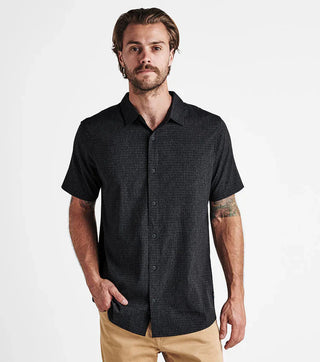 Model wearing the black Roark Bless Up short sleeve button-up shirt.