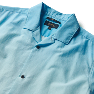Model showcasing the Roark Gonzo Camp Collar Shirt - Hinano Otemanu Light Blue, a Tahiti-inspired piece made from an organic cotton and Tencel blend. This relaxed fit shirt embodies the serene beauty of Bora Bora's Otemanu peak.