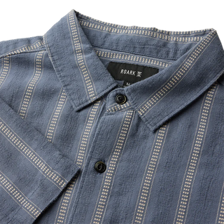 Roark Crosswinds Button Up Shirt in Neptune with blue-grey vertical dobby stripes, short sleeves, a button-front closure, and chest pocket