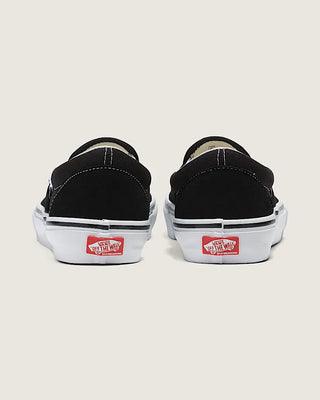 Black slip-on sneakers with red and white labels on a light beige background