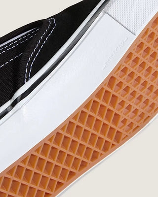 Close-up of a shoe with a white sole, black side panel, and brown textured sole.