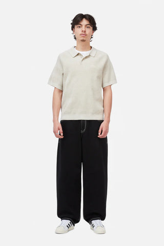 Person wearing a beige short-sleeve shirt and black pants on a white background