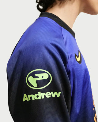 Close-up of a blue and black athletic jersey worn by a model, featuring a green Andrew logo on the sleeve and a yellow Nike swoosh on the chest.