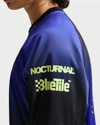 Close-up of a person wearing a blue and black athletic jersey with neon yellow-green 'NOCTURNAL' and 'BlueTile' branding on the back.