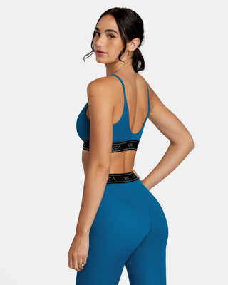 A confident woman wearing the RVCA Base Sports Bra, showing off the racerback design and half-moon back cut-out. The sports bra is made from recycled performance fabric.