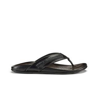 OluKai Mea Ola Mano Sandals in Black/Dark Shadow — premium full-grain leather with hand-woven Polynesian lashing details, laser-etched Mano shark artwork, flexible midsole, and cushioned footbed
