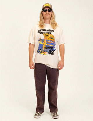 Duvin Tourist Tee in Antique with a colorful beach sunset graphic, a woman in a pink bikini, and Dethawing Tourists lettering