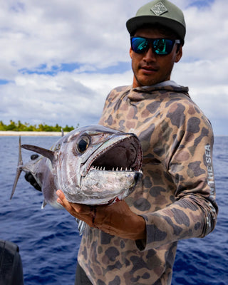 Man holding a large fish by the water with a cloudy sky in the background