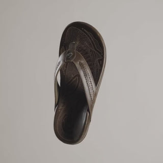 OluKai Mea Ola Mano leather sandals in Dark Java/Mustang with woven straps and shark-inspired etched detailing.
